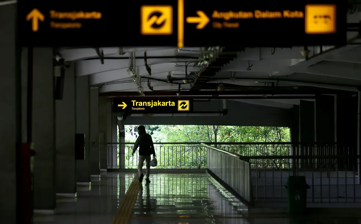 A solitary figure walks through the Transjakarta station in East Jakarta, Indonesia, highlighting urban transit life.