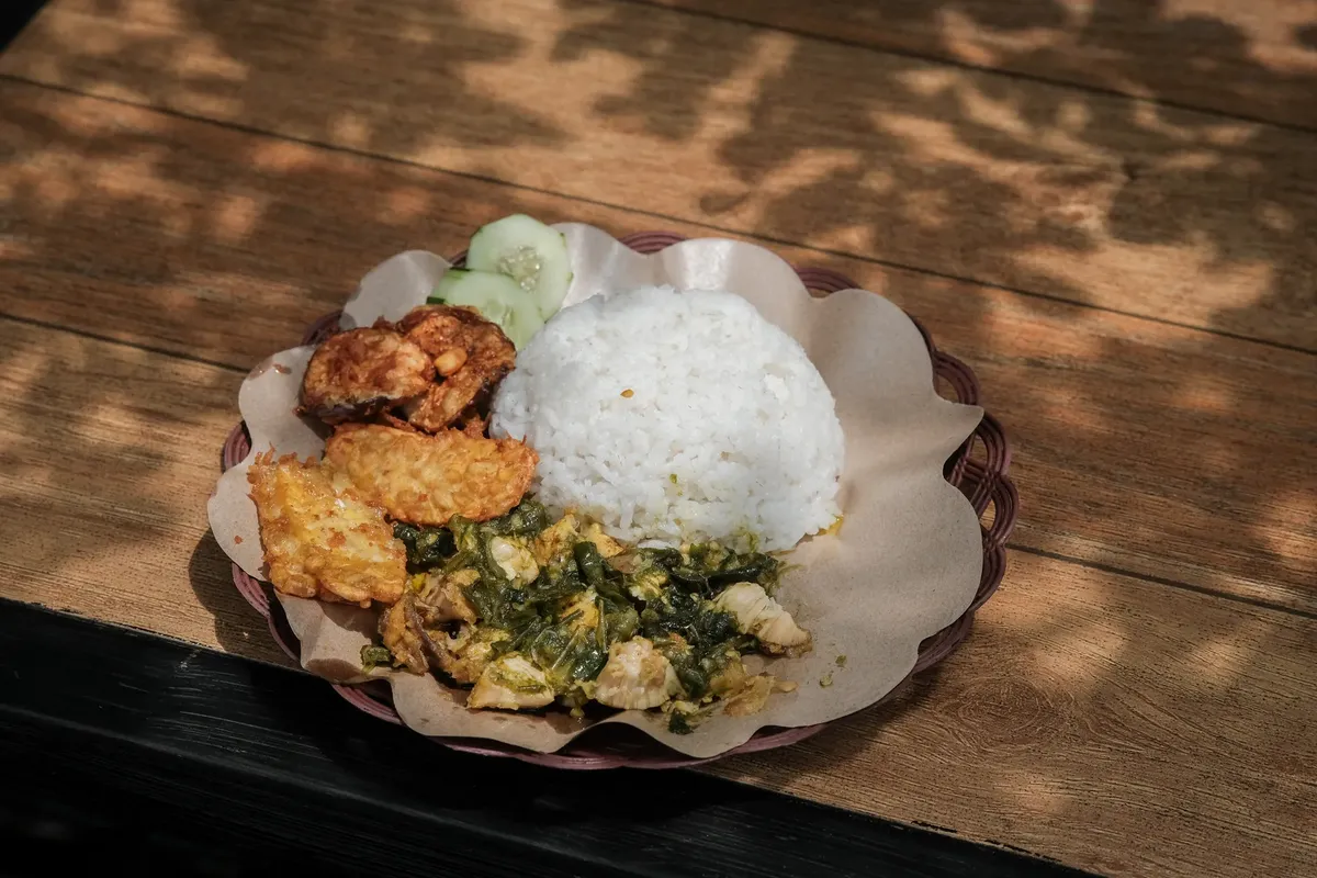 美味しいインドネシアのナシアヤムゲプレクが、スンパル、トペー、そしてキュウリスライスと一緒に木のテーブルに置かれた写真