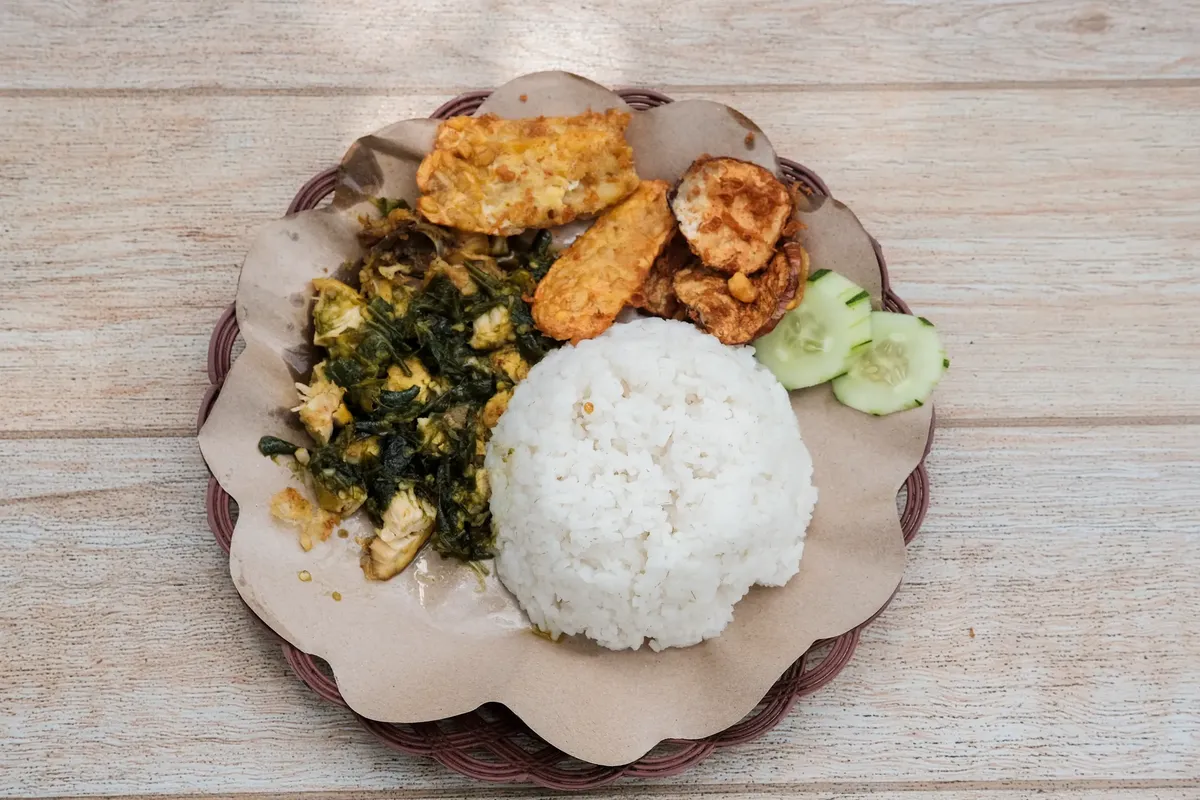 誘惑的なインドネシアのスンパルマッシュドチキンと米、トペー、そしてキュウリスライスが置かれたプレート
