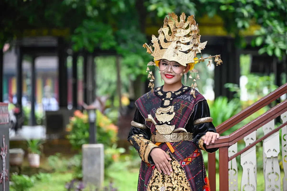 伝統的なインドネシアの服を着た女性が外で活気に満ちた文化遺産を紹介しています。