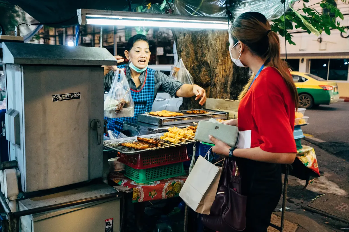 Night market vendor selling grilled street food skewers to a customer. Urban nightlife scene.